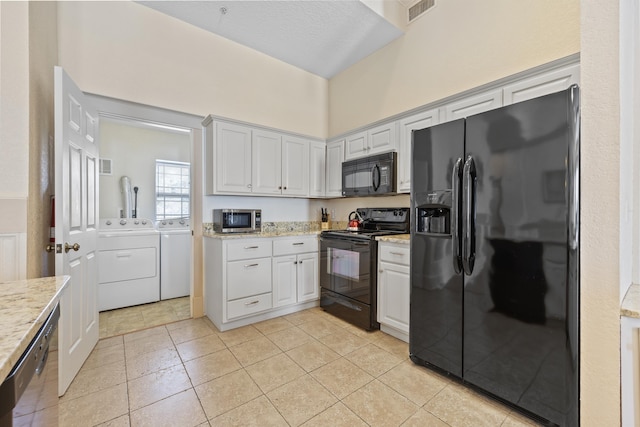 kitchen featuring light stone counters, black appliances, washer and dryer, light tile patterned floors, and white cabinets