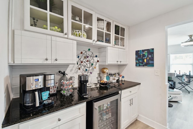 bar featuring wine cooler, white cabinetry, decorative backsplash, and dark stone countertops