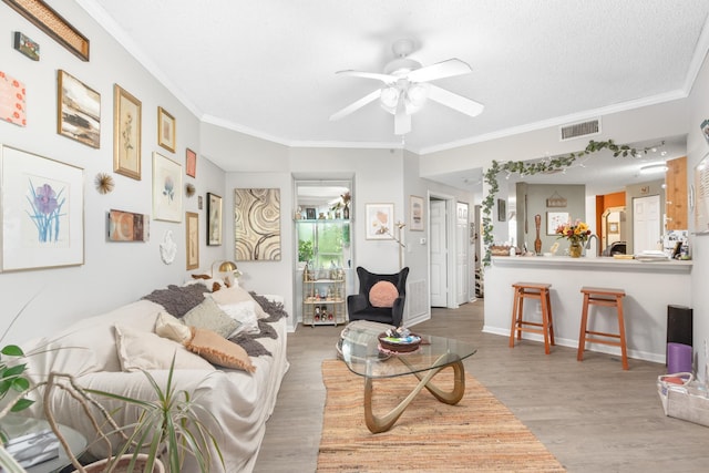 living room with a textured ceiling, ceiling fan, wood-type flooring, and crown molding