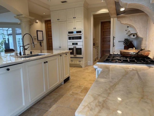 kitchen with gas cooktop, a sink, arched walkways, white double oven, and decorative columns