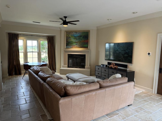 living room featuring stone tile floors, a glass covered fireplace, a ceiling fan, and ornamental molding