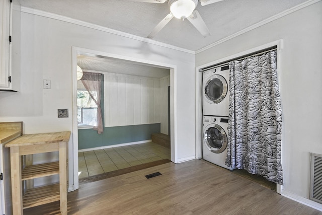 washroom with stacked washer and clothes dryer, wood finished floors, a ceiling fan, ornamental molding, and a textured ceiling