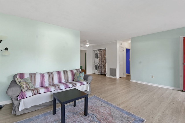 living area with stacked washer and clothes dryer, baseboards, light wood-style floors, and ceiling fan