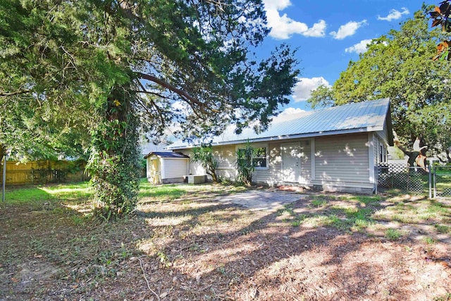 back of property featuring a storage shed, fence, an outdoor structure, metal roof, and central air condition unit