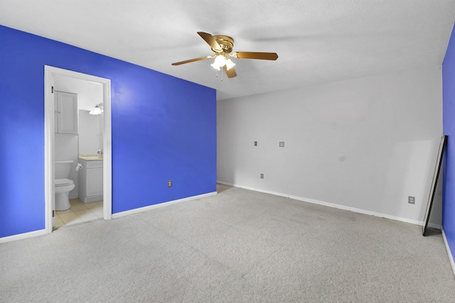 unfurnished bedroom featuring carpet, baseboards, ensuite bathroom, a ceiling fan, and a sink