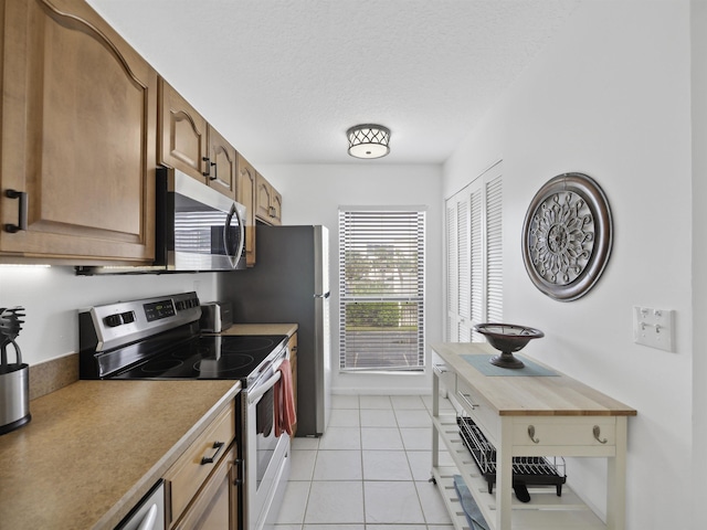 kitchen with butcher block countertops, light tile patterned floors, stainless steel appliances, and a textured ceiling