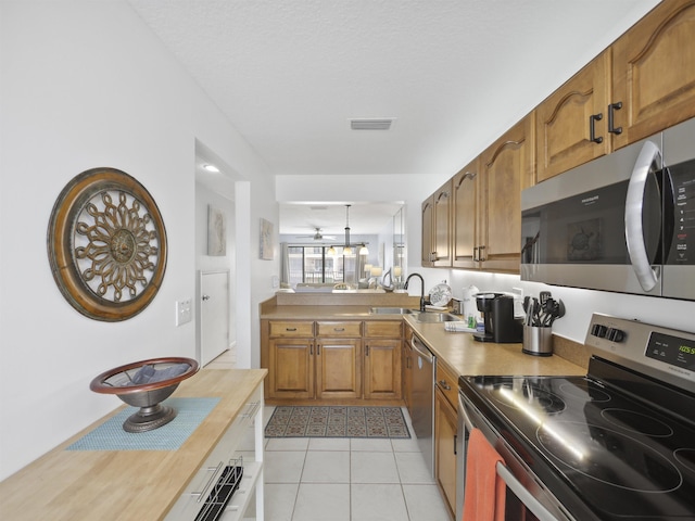 kitchen with sink, ceiling fan, light tile patterned floors, decorative light fixtures, and stainless steel appliances