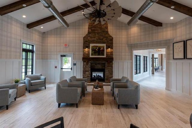 living room featuring french doors, vaulted ceiling with beams, light hardwood / wood-style flooring, and a stone fireplace