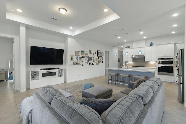 living room with light tile patterned floors, sink, and a tray ceiling