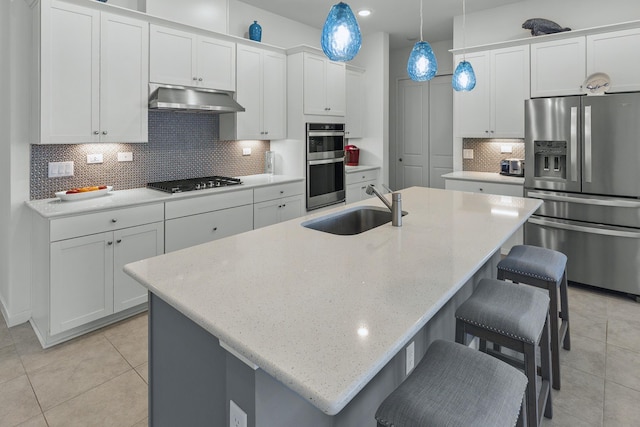 kitchen featuring tasteful backsplash, stainless steel appliances, a kitchen island with sink, sink, and pendant lighting