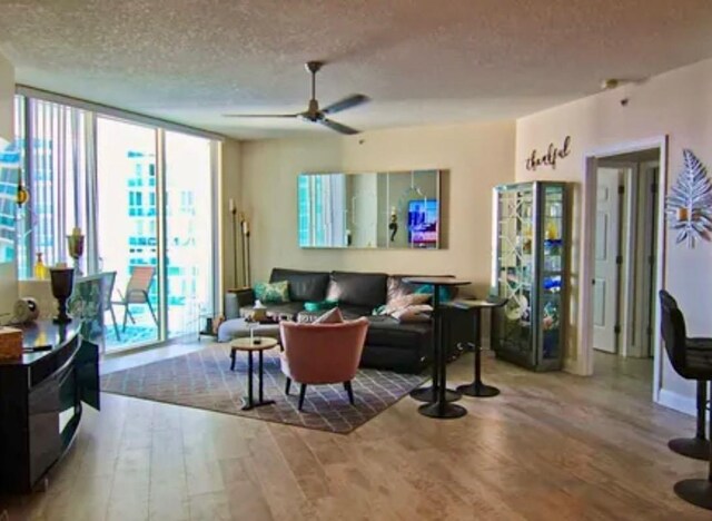 living room featuring ceiling fan, hardwood / wood-style floors, a textured ceiling, and a wall of windows