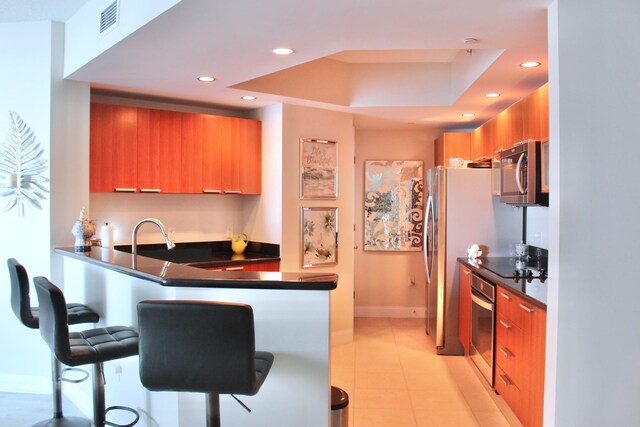 kitchen with kitchen peninsula, appliances with stainless steel finishes, a kitchen breakfast bar, a raised ceiling, and sink