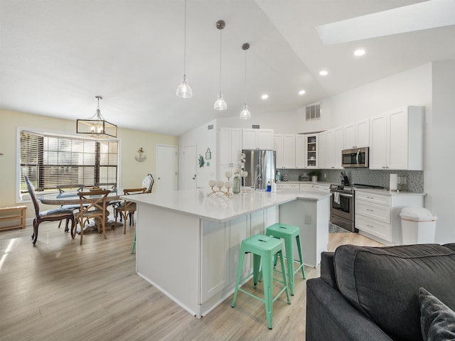 kitchen with backsplash, a kitchen island with sink, light hardwood / wood-style flooring, appliances with stainless steel finishes, and decorative light fixtures