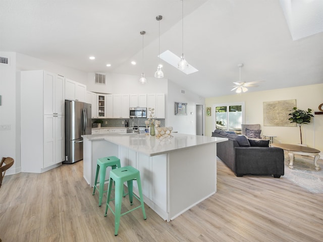 kitchen featuring lofted ceiling with skylight, white cabinets, a spacious island, light wood-type flooring, and stainless steel appliances