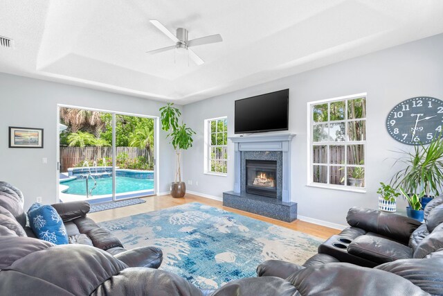 living room with hardwood / wood-style flooring, ceiling fan, a high end fireplace, and a tray ceiling