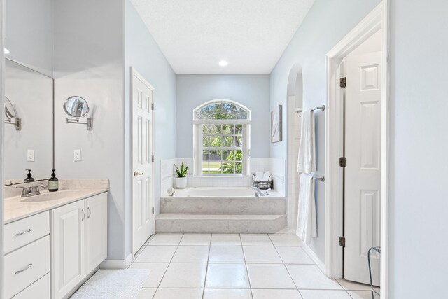 bathroom with tile patterned floors, a textured ceiling, vanity, and tiled tub