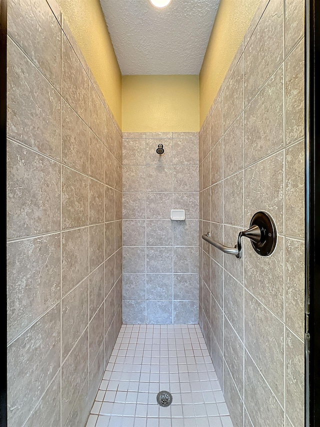 bathroom featuring tiled shower, a textured ceiling, and tile walls