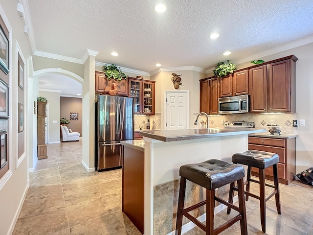 kitchen with appliances with stainless steel finishes, tasteful backsplash, ornamental molding, a breakfast bar, and a center island with sink