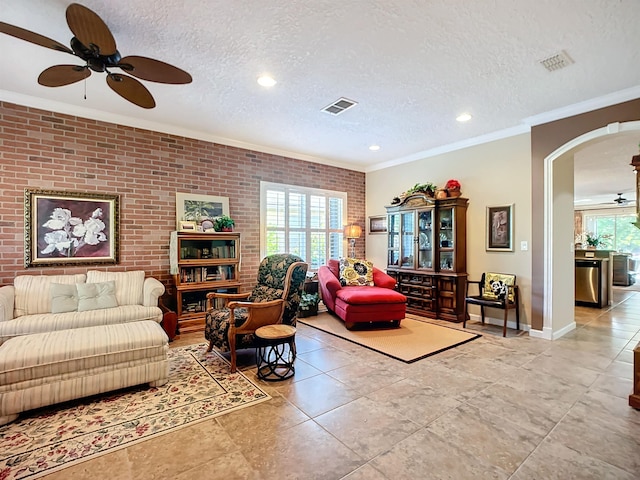 tiled living room featuring plenty of natural light, brick wall, a textured ceiling, and ornamental molding