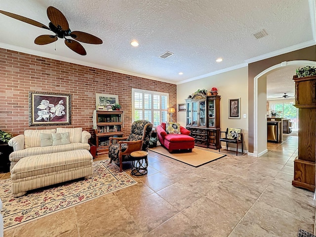 living room with ceiling fan, brick wall, a textured ceiling, and a wealth of natural light