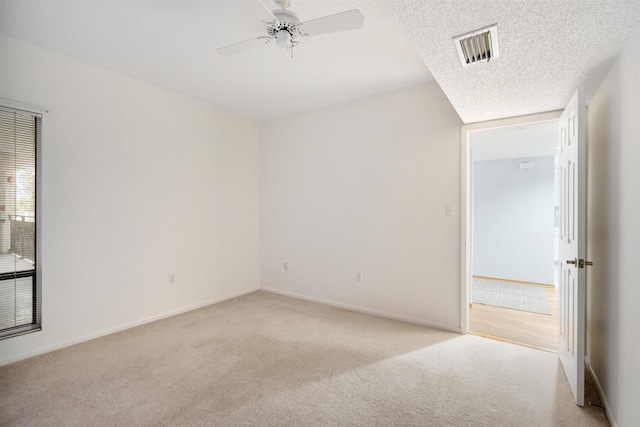 spare room with a textured ceiling, light colored carpet, and ceiling fan