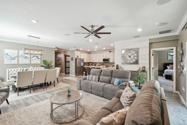 living area featuring ornamental molding, visible vents, light wood-style floors, and a textured ceiling