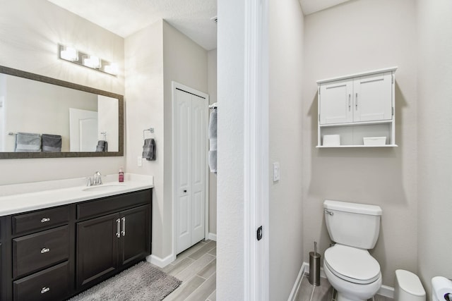 bathroom featuring baseboards, toilet, wood tiled floor, vanity, and a closet