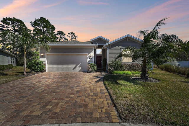 view of front of house featuring decorative driveway, a lawn, and an attached garage