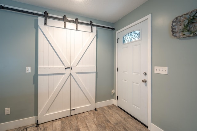 foyer with a barn door, wood finished floors, and baseboards