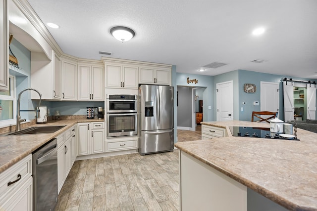 kitchen with a barn door, light wood-style flooring, a sink, visible vents, and appliances with stainless steel finishes