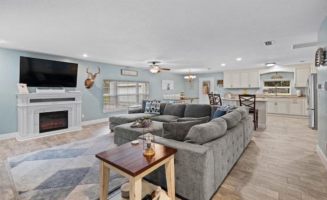 living area with visible vents, a glass covered fireplace, light wood-style flooring, and recessed lighting