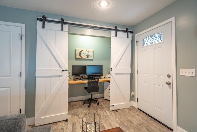 office area featuring light wood-style floors, a barn door, baseboards, and a textured ceiling