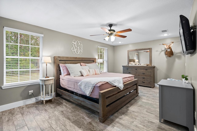 bedroom with baseboards, a ceiling fan, visible vents, and light wood-style floors