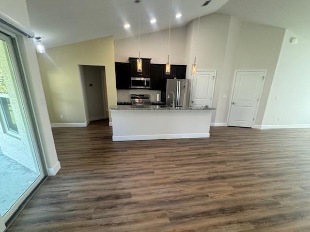 kitchen with stainless steel appliances, an island with sink, light stone counters, high vaulted ceiling, and dark hardwood / wood-style flooring