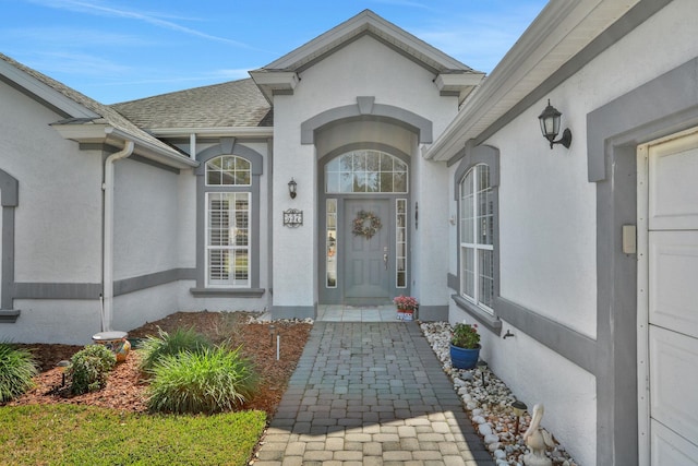 doorway to property with a shingled roof and stucco siding