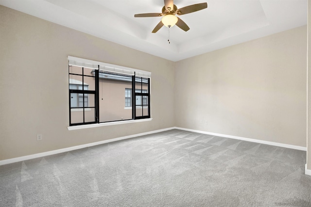 carpeted empty room with a raised ceiling and ceiling fan