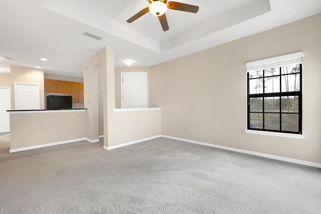 carpeted spare room with ceiling fan and a raised ceiling