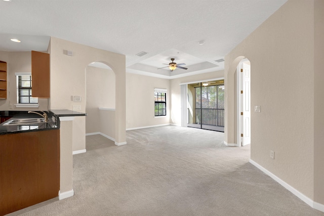 unfurnished living room with ceiling fan, sink, light carpet, and a tray ceiling