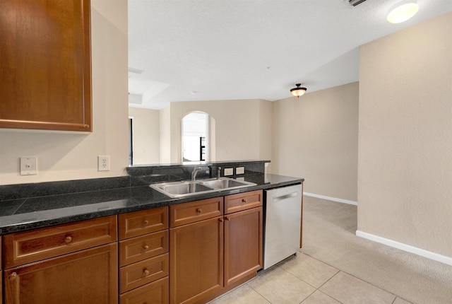 kitchen featuring dark stone countertops, dishwasher, sink, and light tile patterned floors