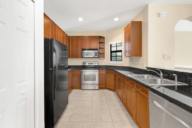 kitchen with sink, stainless steel appliances, dark stone counters, a textured ceiling, and light tile patterned floors