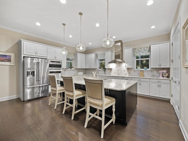 kitchen featuring decorative light fixtures, stainless steel appliances, a center island with sink, and wall chimney range hood