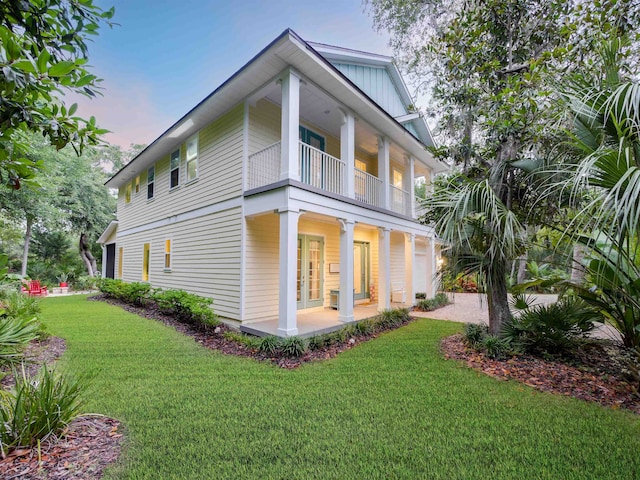 back house at dusk with a balcony, a yard, and french doors