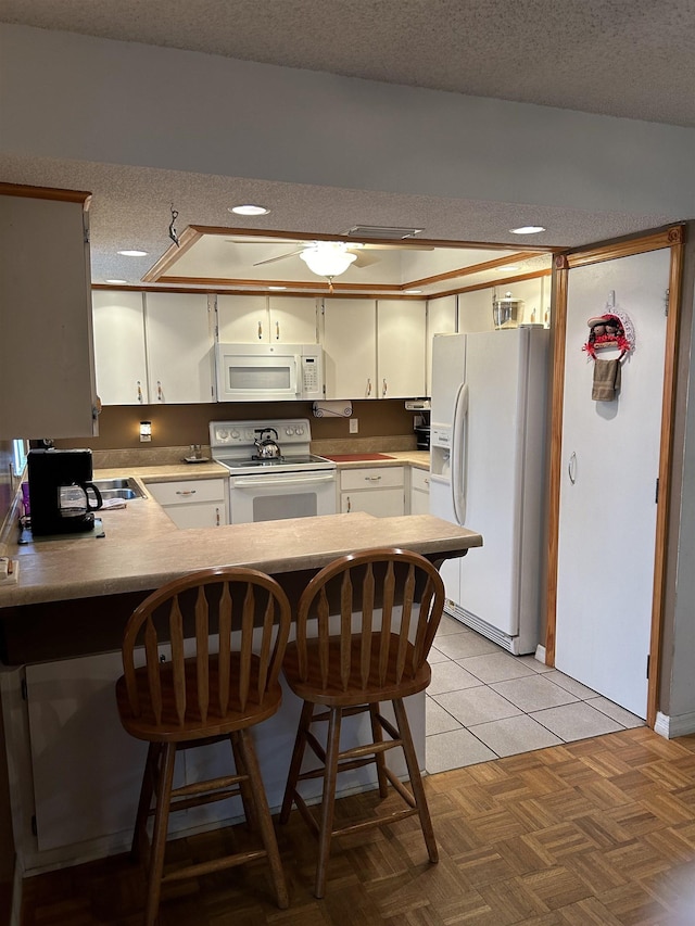 1417 Golf Ave, Ormond Beach, FL 32174 - kitchen with white appliances, a peninsula, a textured ceiling, white cabinetry, and a breakfast bar area