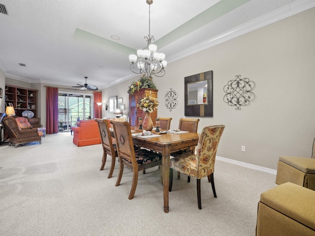 carpeted dining room with ceiling fan with notable chandelier, a tray ceiling, and ornamental molding