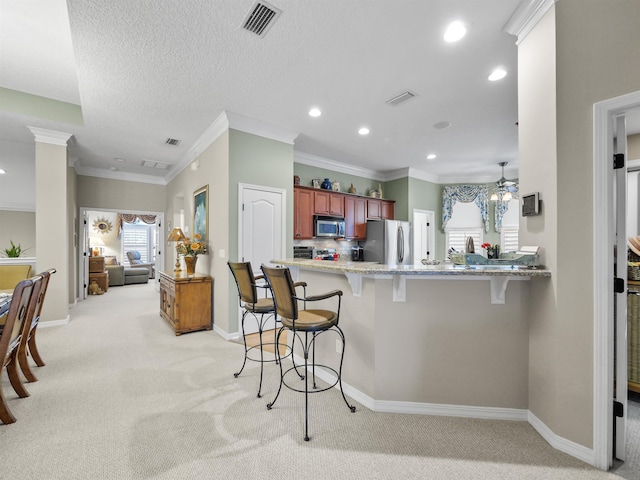 kitchen with light carpet, ceiling fan, a kitchen bar, kitchen peninsula, and stainless steel appliances