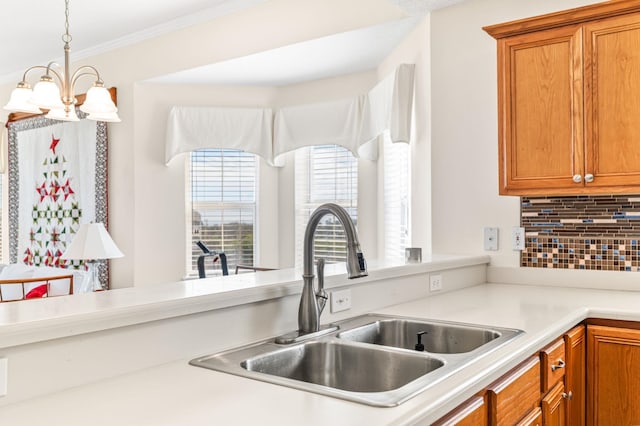 kitchen with sink, hanging light fixtures, an inviting chandelier, tasteful backsplash, and crown molding