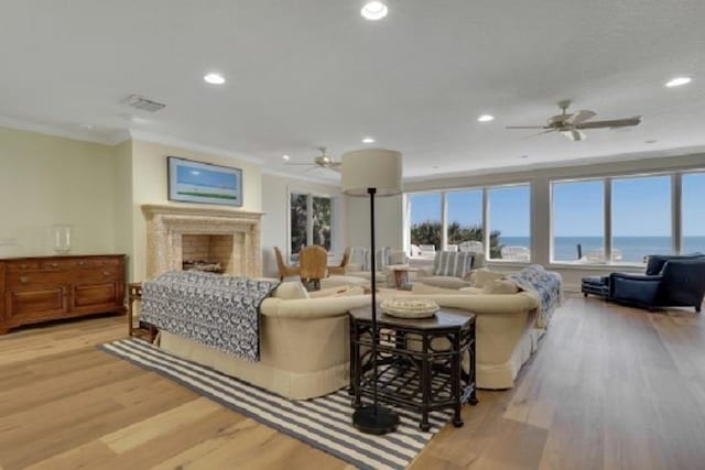 living room featuring light wood-type flooring, a water view, ceiling fan, and ornamental molding