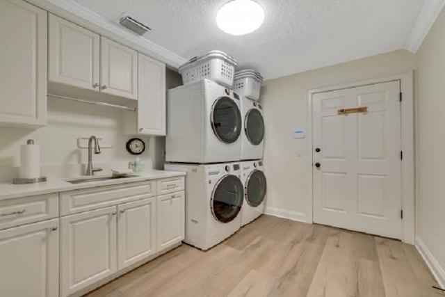 washroom with cabinets, sink, light wood-type flooring, a textured ceiling, and stacked washer / drying machine