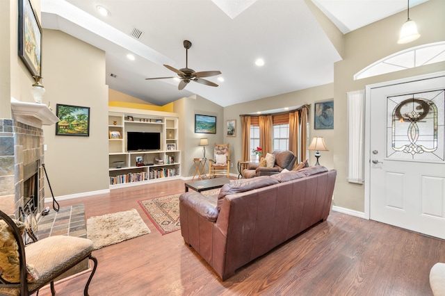 living room with ceiling fan, a tiled fireplace, built in shelves, hardwood / wood-style floors, and lofted ceiling