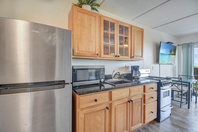 kitchen with sink, light brown cabinets, stainless steel appliances, light hardwood / wood-style flooring, and dark stone countertops